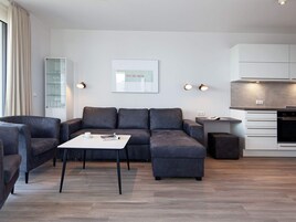 Ein modernes Wohnzimmer mit einem Ecksofa, einem Couchtisch und einer Küchenzeile inklusive Einbauofen.