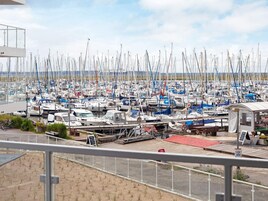 A marina with numerous boats docked, a small building, and a sandy area with a fence.
