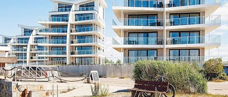 A modern multi-story residential building with balconies, a dock, and a bench.