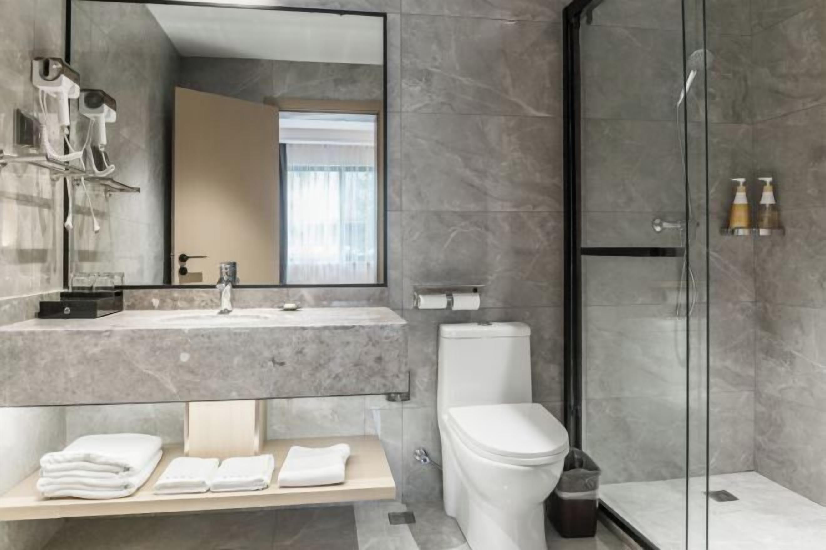 Un baño moderno con lavamanos de mármol, inodoro, cabina de ducha de vidrio y un banco con toallas.