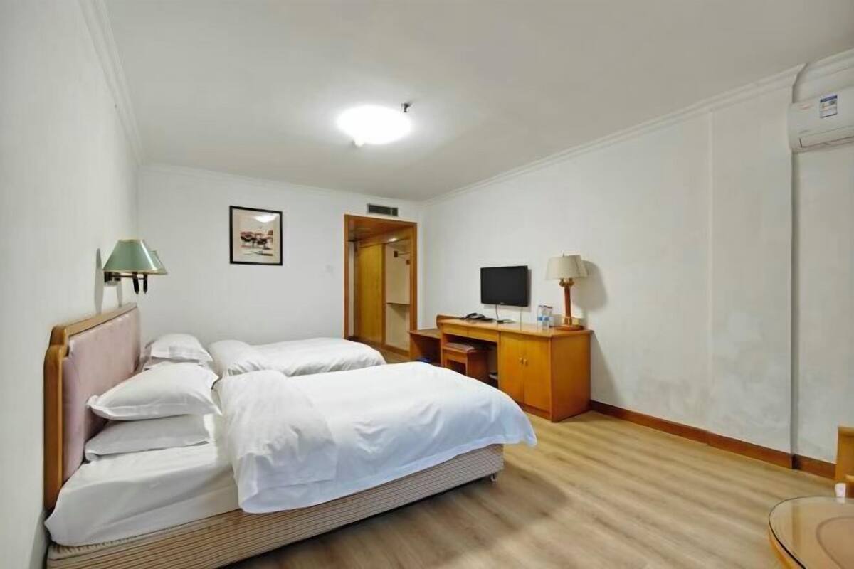 Hotellihuone, jossa on kaksi sänkyä, työpöytä, televisio ja peili.