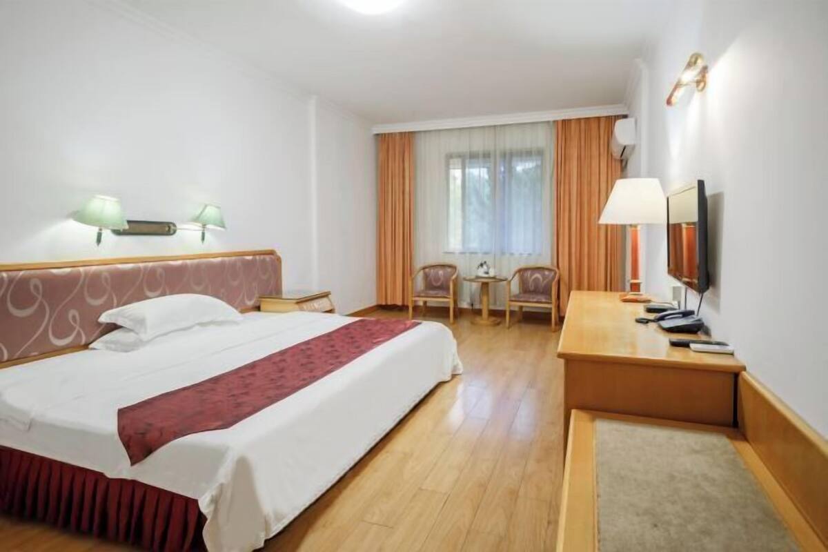Hotellihuone, jossa on suuri sänky, työpöytä lampun kanssa, tuoli ja televisio.