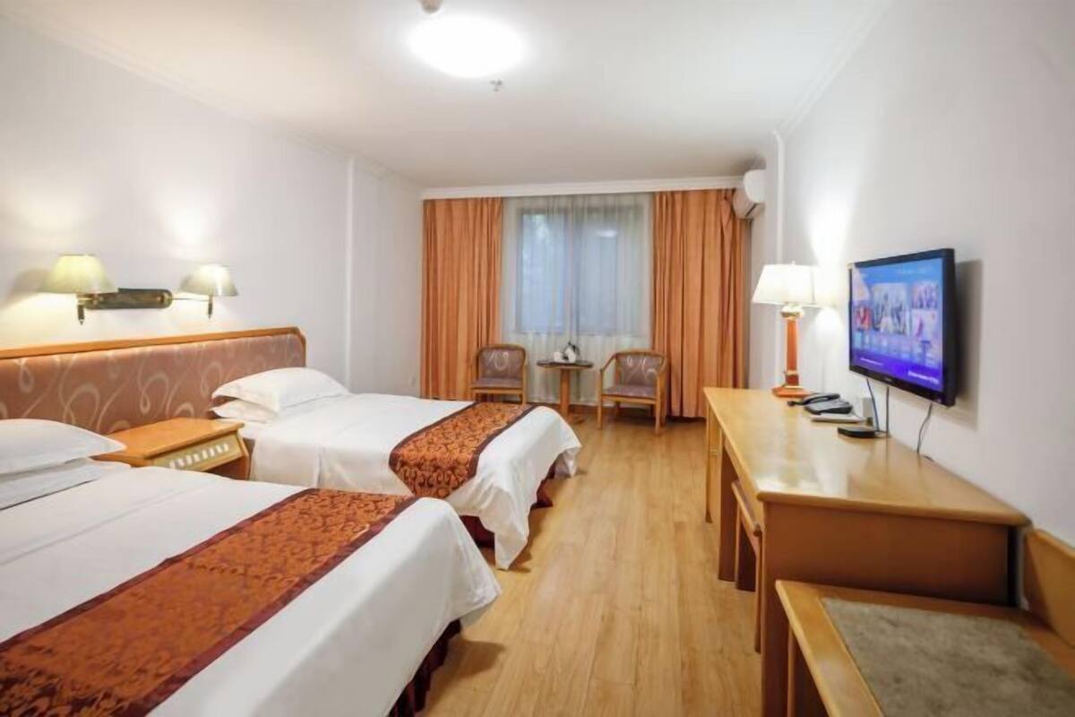 Hotellihuone, jossa on kaksi sänkyä, työpöytä, televisio ja ikkuna, jossa on verhot.