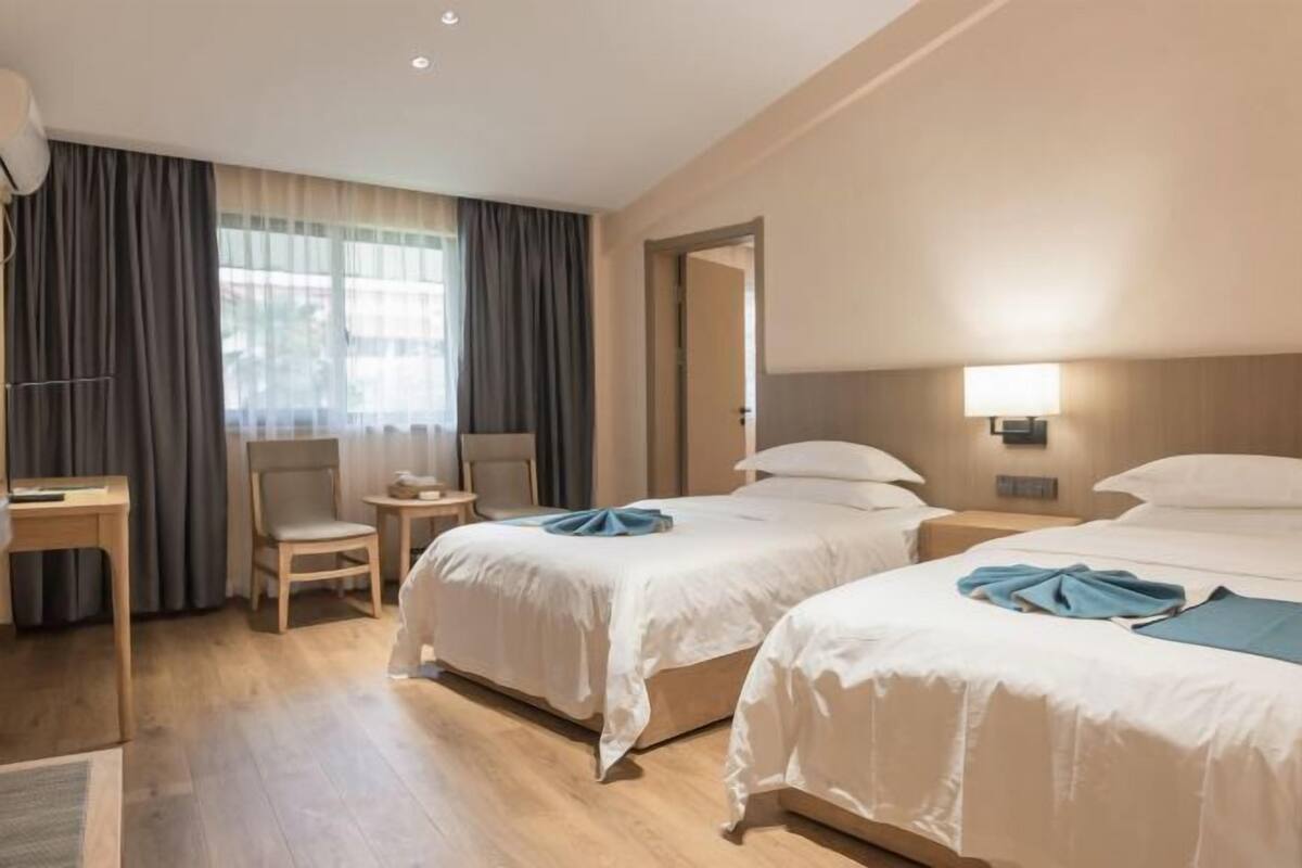 Hotellihuone, jossa on kaksi sänkyä, työpöytä, tuoli ja ikkuna, jossa on verhot.