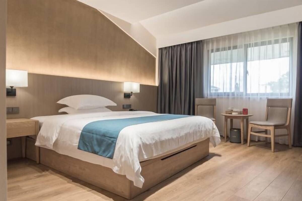 Moderni hotellihuone, jossa on suuri sänky, yöpöydät, pieni pöytä ja tuoli.
