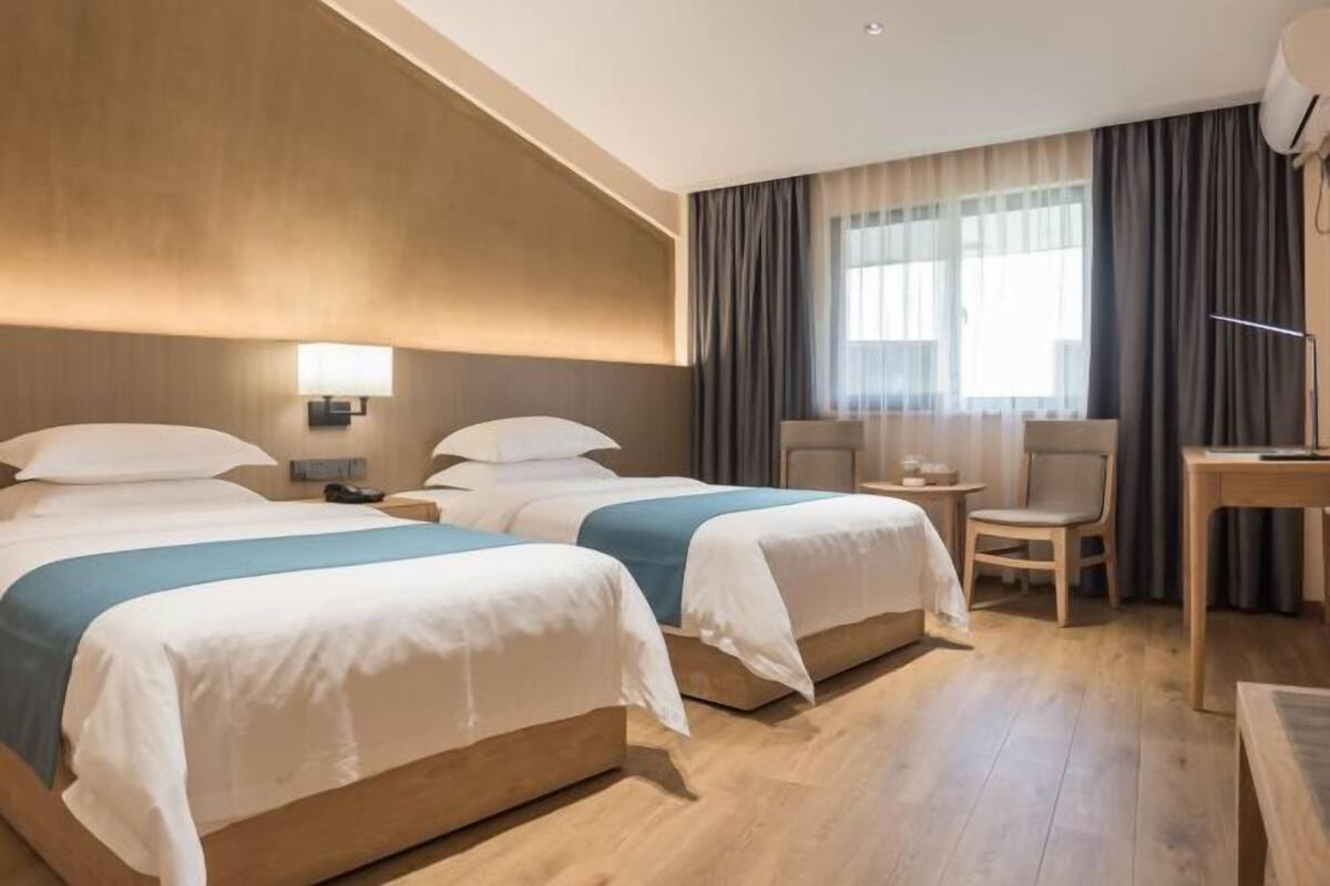 Hotellihuone, jossa on kaksi sänkyä, työpöytä, tuoli ja lamppu.