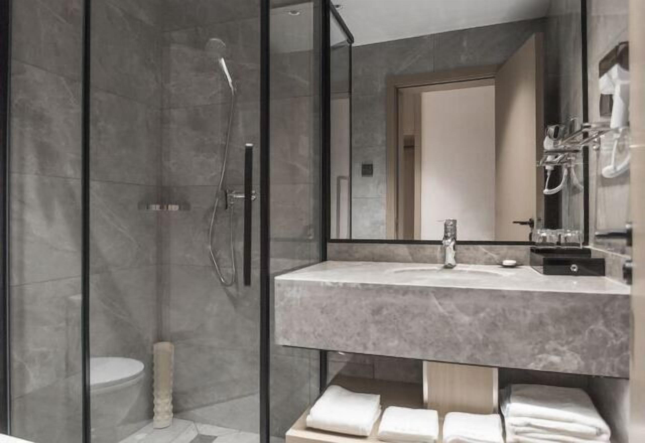 Un baño moderno con ducha de vidrio, lavabo de mármol y un espejo grande.