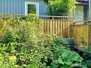Une terrasse en bois, entourée d’une clôture en bois, de plantes luxuriantes et d’une maison avec une fenêtre.