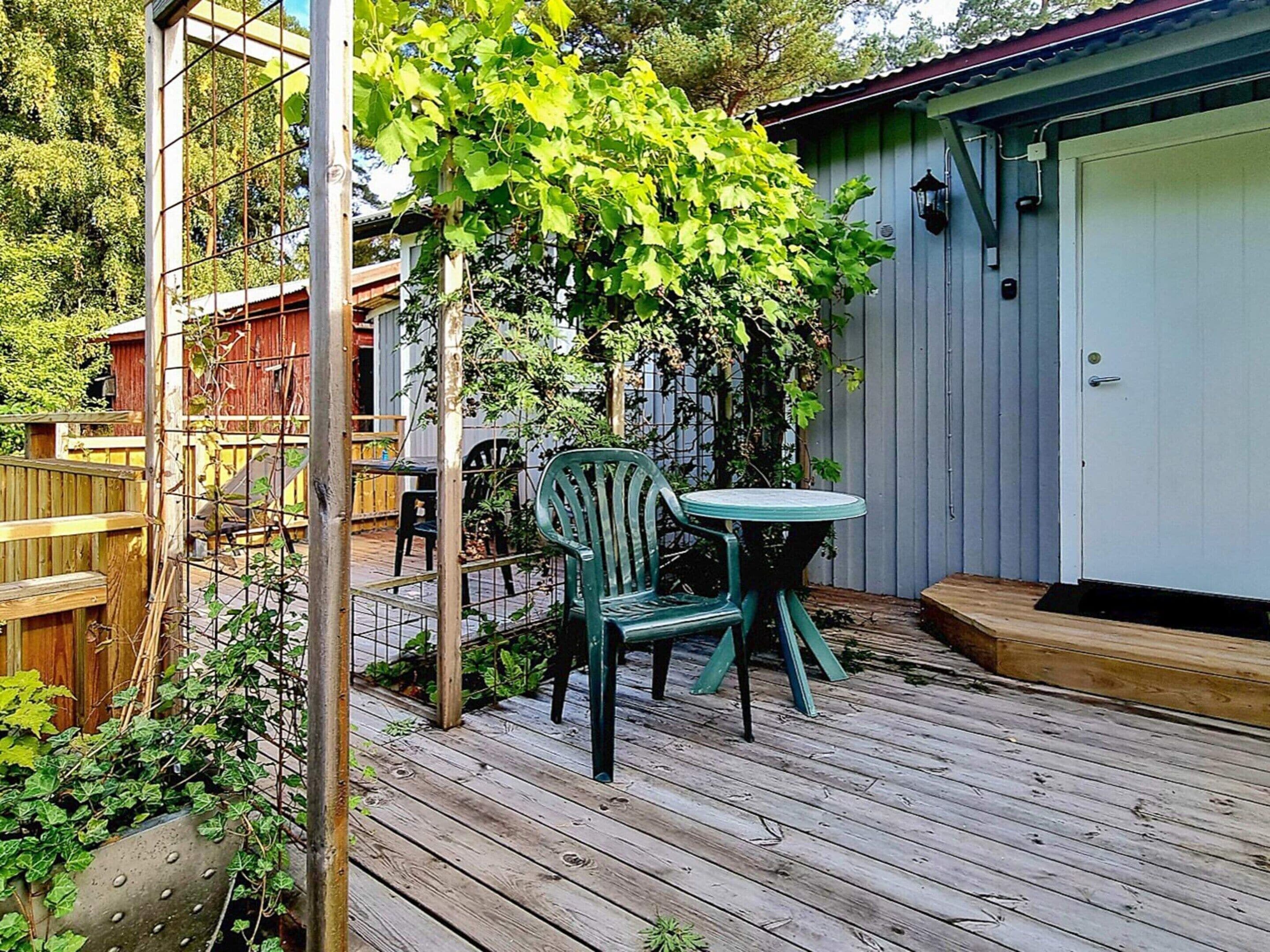 Una terraza de madera con una silla y mesa verdes, una valla de metal y un edificio con una puerta blanca.