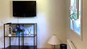 A room with a mounted television, a black console table with decorative items, a standing lamp, and a window with a potted plant. - 4 Person Holiday Home in Uddevalla (Uddevalla)