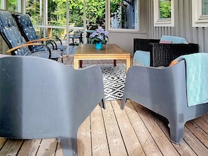 A covered outdoor seating area with two grey chairs, a wooden table, and a potted plant. - 4 Person Holiday Home in Uddevalla (Uddevalla)
