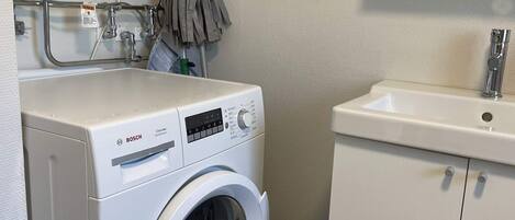 A compact washing machine with a digital display, a sink with a faucet, and a towel rack.