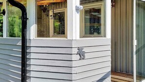 A white building with a porch, a window with a wooden beam, and a door with a glass panel. - 4 Person Holiday Home in Uddevalla (Uddevalla)