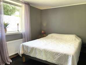 A bedroom with a single bed, a window with curtains, a radiator, and a small plant on the windowsill.