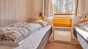 A room with two beds, a window with curtains, a bedside lamp, and a radiator. - 4 Person Holiday Home in Aakirkeby (Akirkeby)