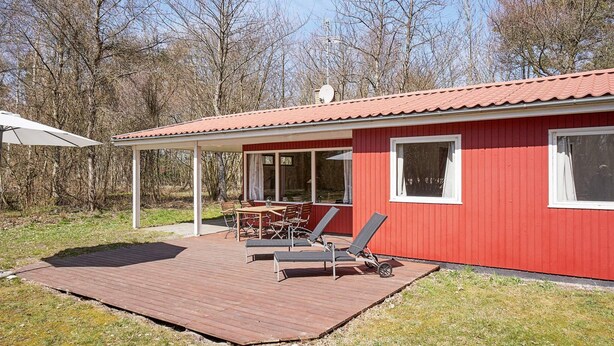 A red building with a covered patio, outdoor furniture, and a view of leafless trees. - 4 Person Holiday Home in Aakirkeby (Akirkeby)