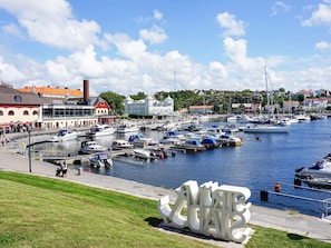 A marina with boats docked, a large white sculpture, and buildings in the background.