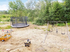 A sandy outdoor area with a trampoline, swing set, and a toy vehicle.