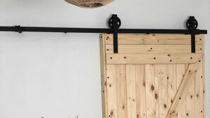 A wooden sliding barn door with a black metal track and a woven basket with dried plants beside it.