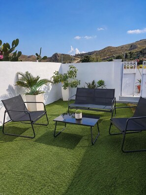 Un área de estar al aire libre con sofá, sillas, césped artificial y plantas en macetas.