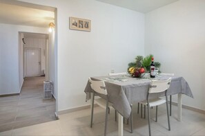 Uma sala de jantar com mesa posta para quatro pessoas, uma garrafa de vinho e uma cesta de frutas.