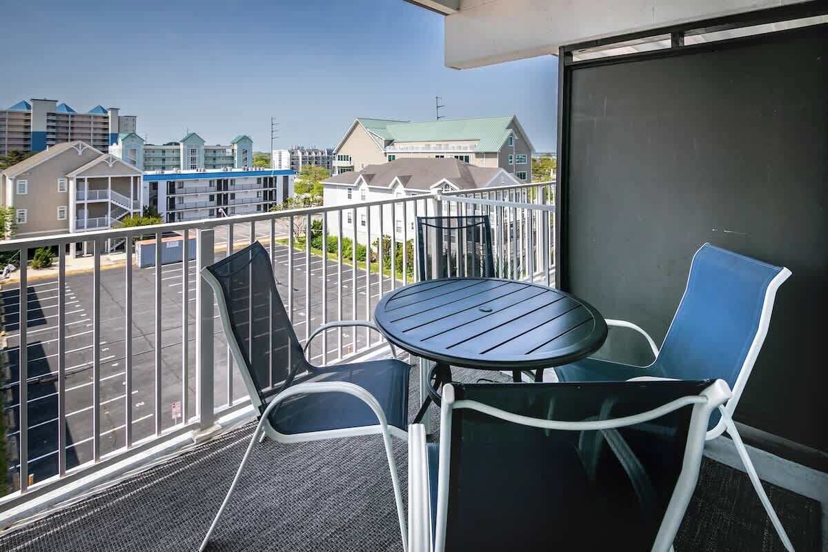 Ein Balkon mit Tisch und Stühlen, mit Blick auf einen Parkplatz und Gebäude.
