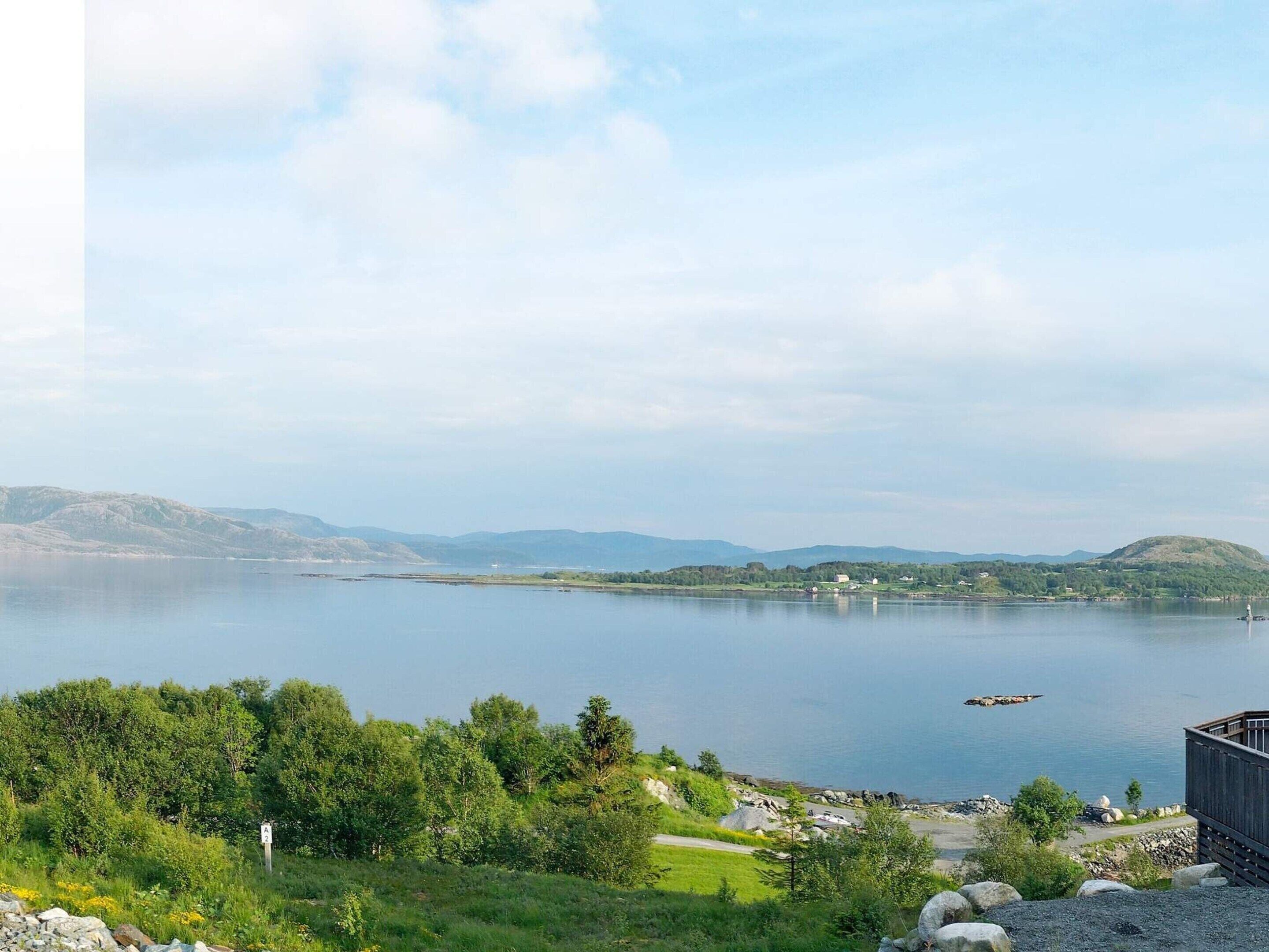 Blick auf einen See mit einer Holzsteganlage, ruhigem Wasser und sanften Hügeln im Hintergrund.