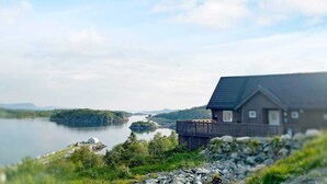 Una baita sul lago con una veranda che si affaccia sull'acqua, immersa nel verde e sotto un cielo sereno.
