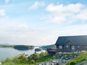 A lakeside cabin with a deck overlooking the water, surrounded by greenery and a clear sky. - 4 Star Holiday Home in Leka (Leka)