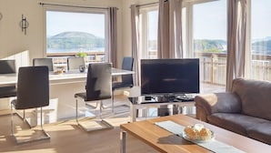 Un soggiorno moderno con TV, divano, zona pranzo e ampie finestre che offrono una vista panoramica.
