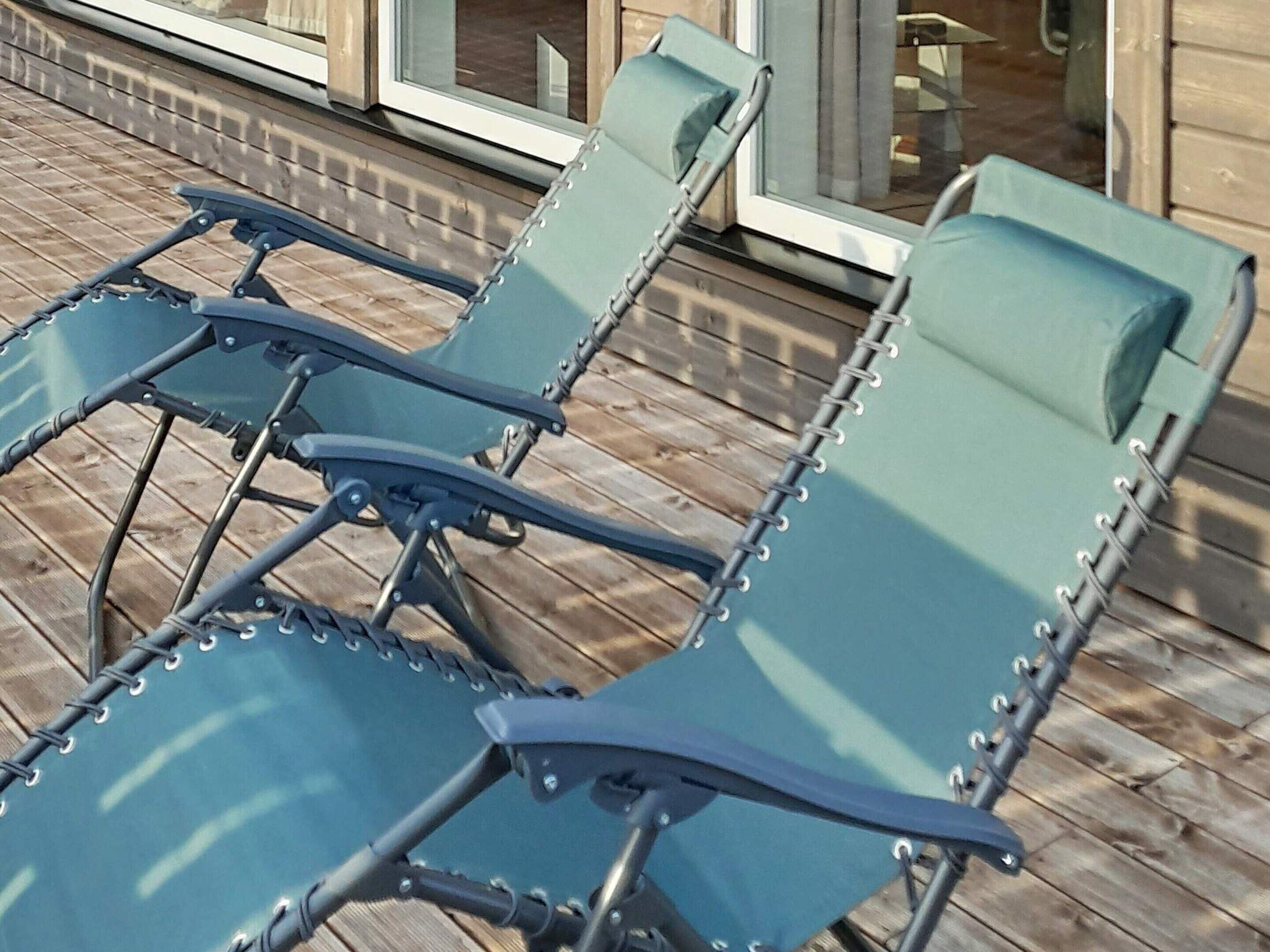 A row of outdoor lounge chairs with metal frames and green cushions, arranged on a wooden deck.