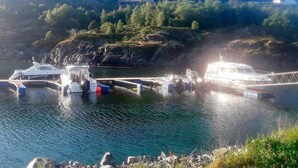 Una marina con barche ormeggiate, un molo che si protende su acque calme e una casa su una collina sullo sfondo.