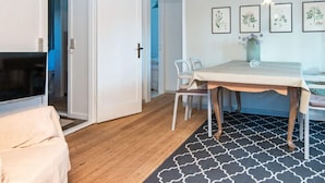 Habitació amb sostre de fusta, taula de dinar amb caires, televisió i estampes botàniques emmarcades a la paret.