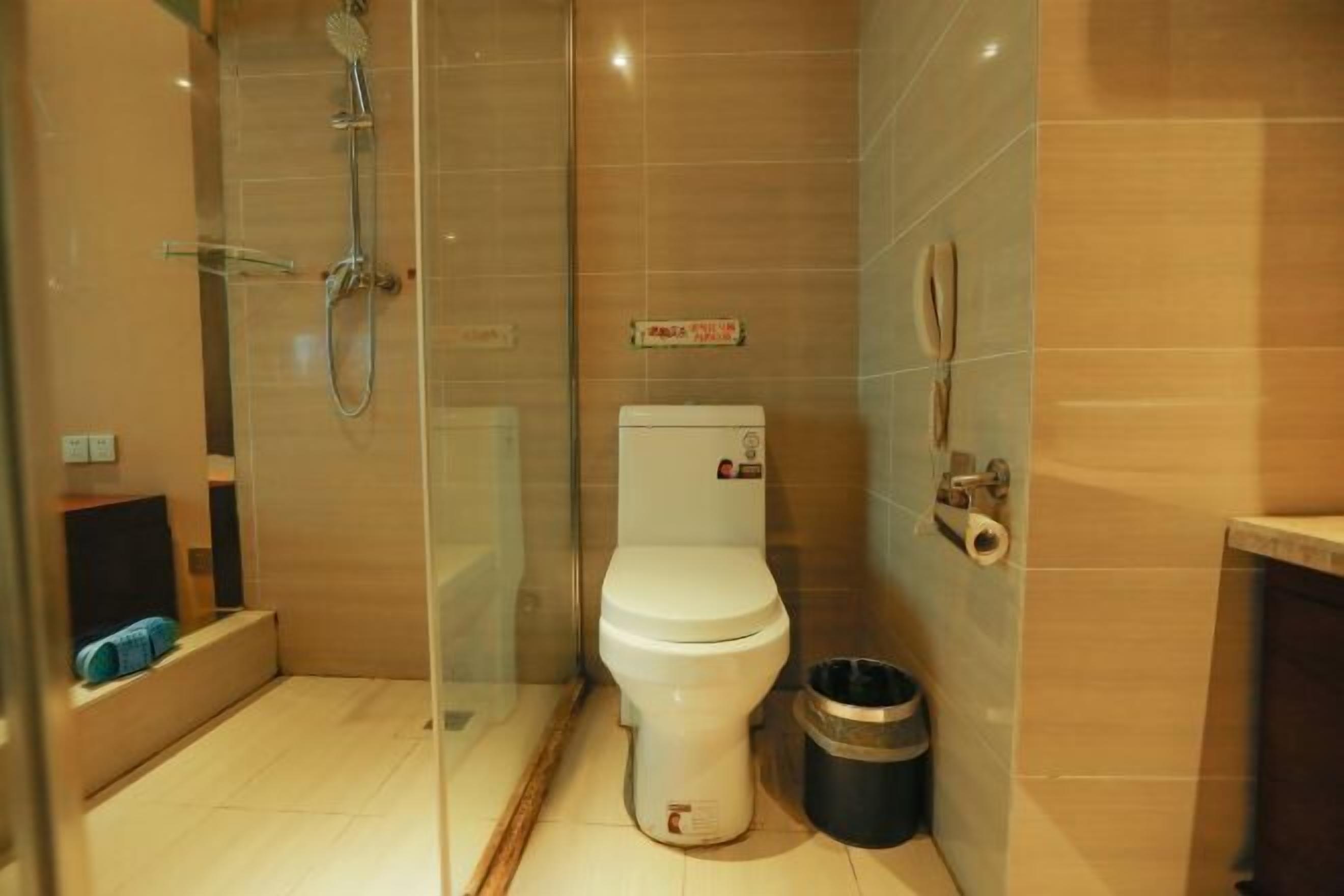 A modern bathroom with a glass-enclosed shower, a toilet, and a trash bin.