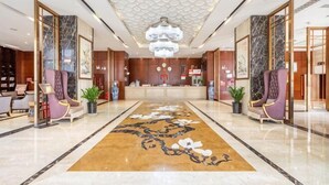 Un vestíbulo de hotel con mostrador de recepción, áreas de estar, una alfombra estampada y un candelabro.