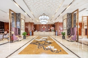 Un hall d’hôtel comprenant un comptoir d’accueil, des espaces détente, une moquette à motifs et un lustre.