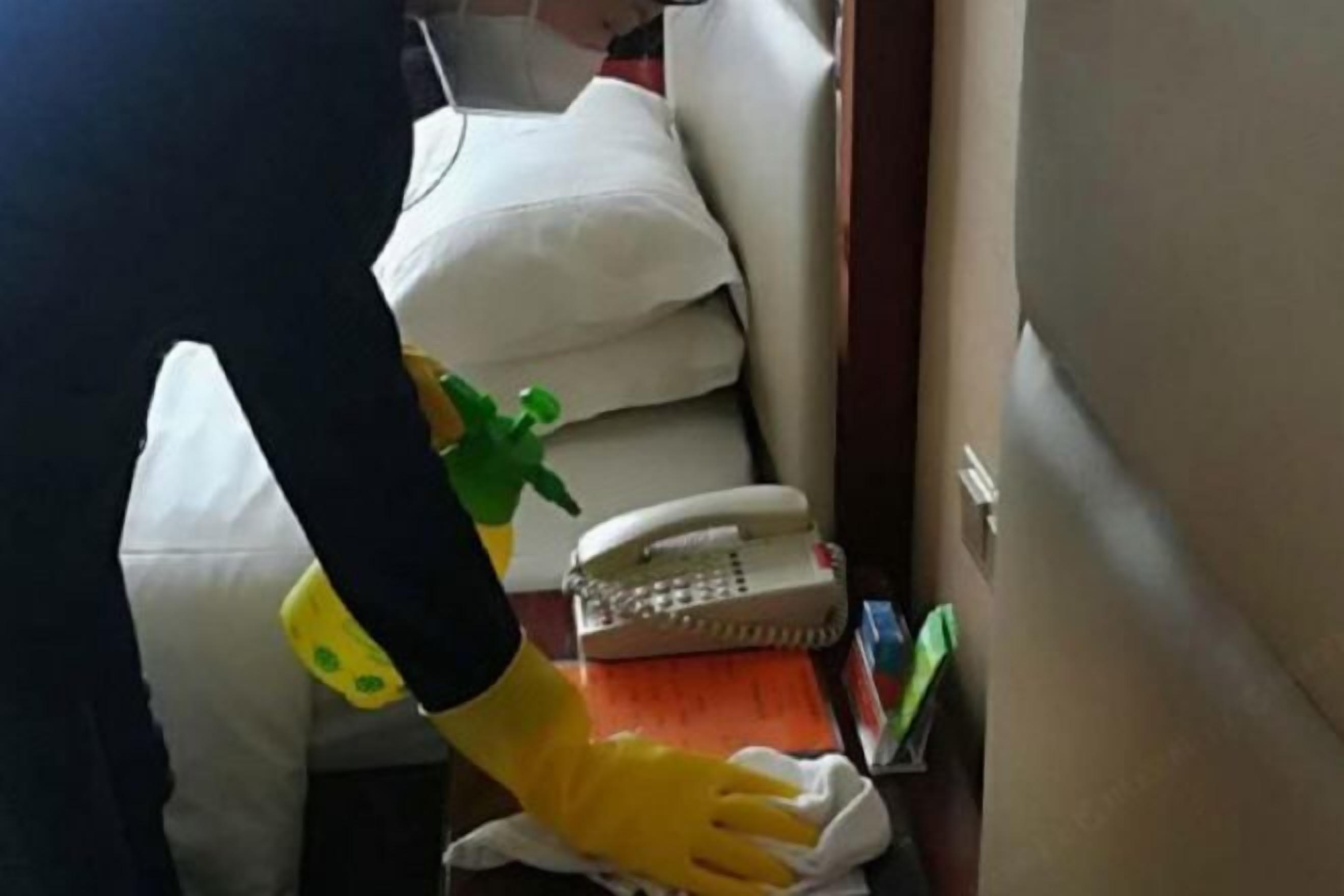 A person cleaning a white sofa with a spray bottle and cloth.