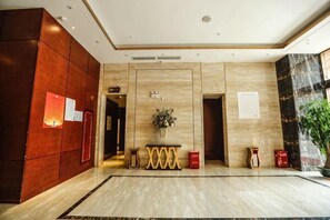 Un hall d’entrée avec un sol en marbre, des boiseries, un comptoir d’accueil et une plante en pot.