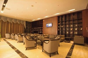 A hotel lobby with a seating area, a television mounted on the wall, and a bookshelf.