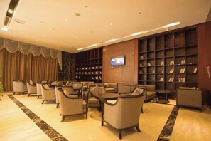 Een hotel lobby met een zithoek, een aan de muur bevestigde televisie en een boekenkast.