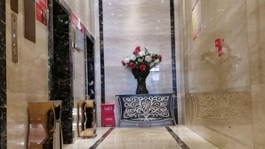 Un vestíbulo de mármol con un mostrador de recepción, un jarrón de flores y un panel decorativo en la pared.