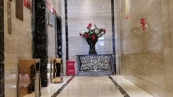 A marble lobby with a reception desk, a vase of flowers, and a decorative wall panel.