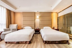 A hotel room with two beds, a sitting area with a chair, a large window, and a glass shower area.