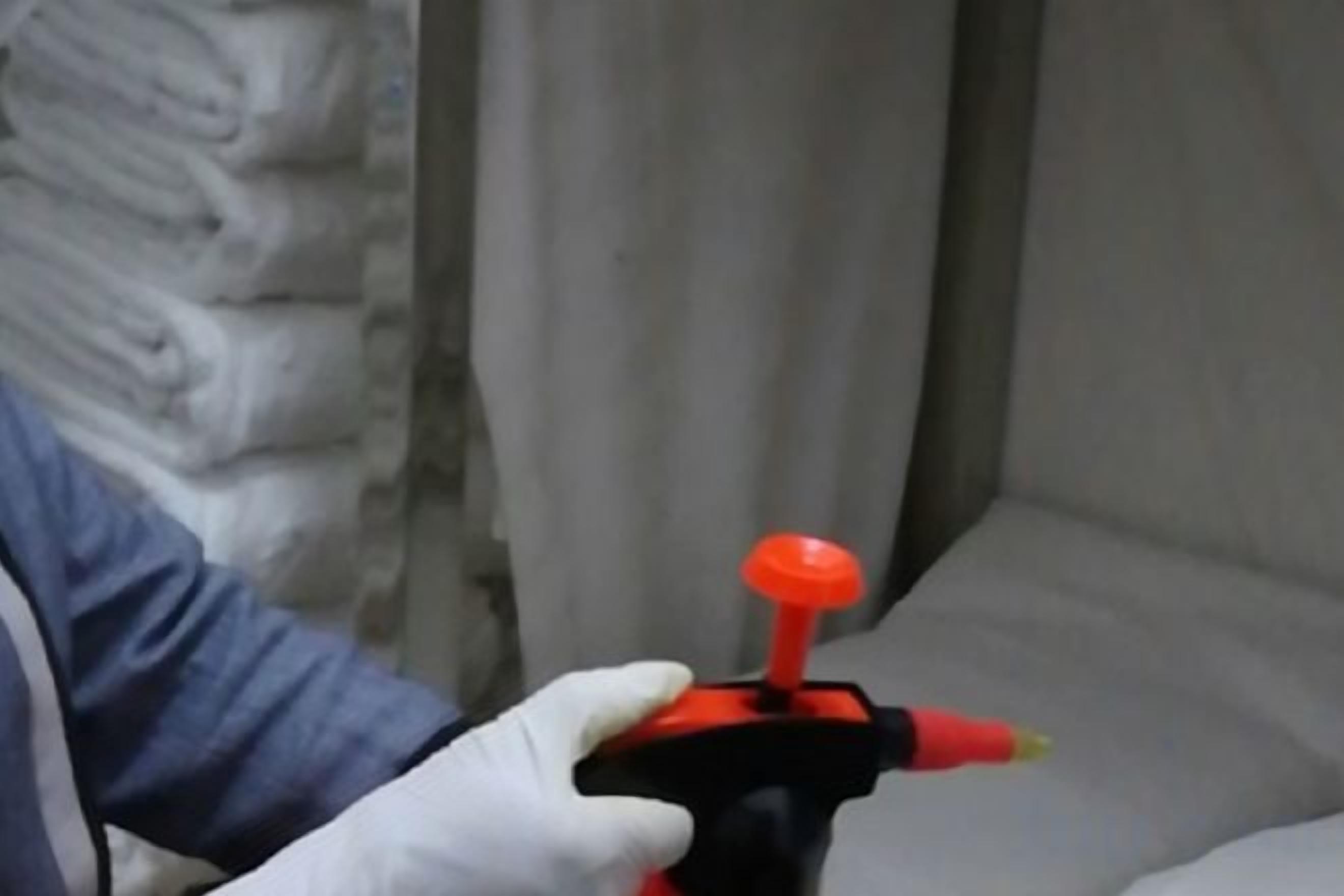 Une personne tenant un objet rouge et noir, qui pourrait être un outil ou un appareil, dans une pièce où se trouve un rideau blanc.