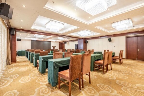 Un salón de conferencias con varias mesas y sillas, piso alfombrado y un techo alto con iluminación empotrada.