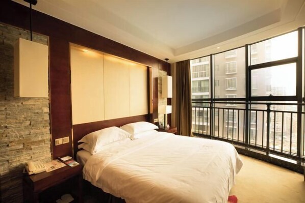 A hotel room with a large bed, a nightstand, a lamp, and a view of the city through large windows.