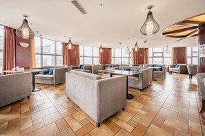 Un vestíbulo amplio con varias zonas de estar, ventanas grandes y luminarias modernas.