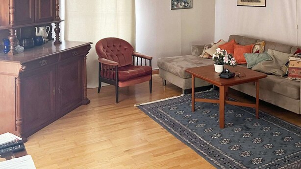 Un salon comprenant un meuble en bois, un fauteuil rouge, un canapé, une table basse et un tapis à motifs.