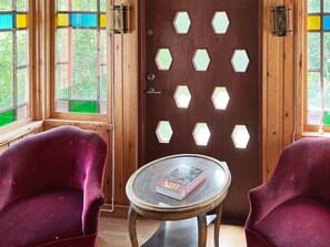 A room with a wooden door featuring hexagonal windows, two plush red chairs, and a small round table with a book. - 7 Person Holiday Home in Algaras (Älgarås)