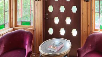 Una habitación con puerta de madera, ventanas hexagonales, dos sillones cómodos y una pequeña mesa redonda con un libro.